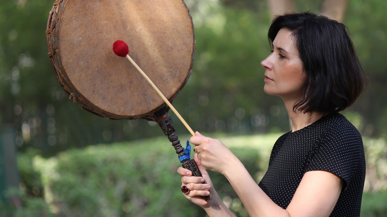 Magdalena playing a frame drum in a garden
