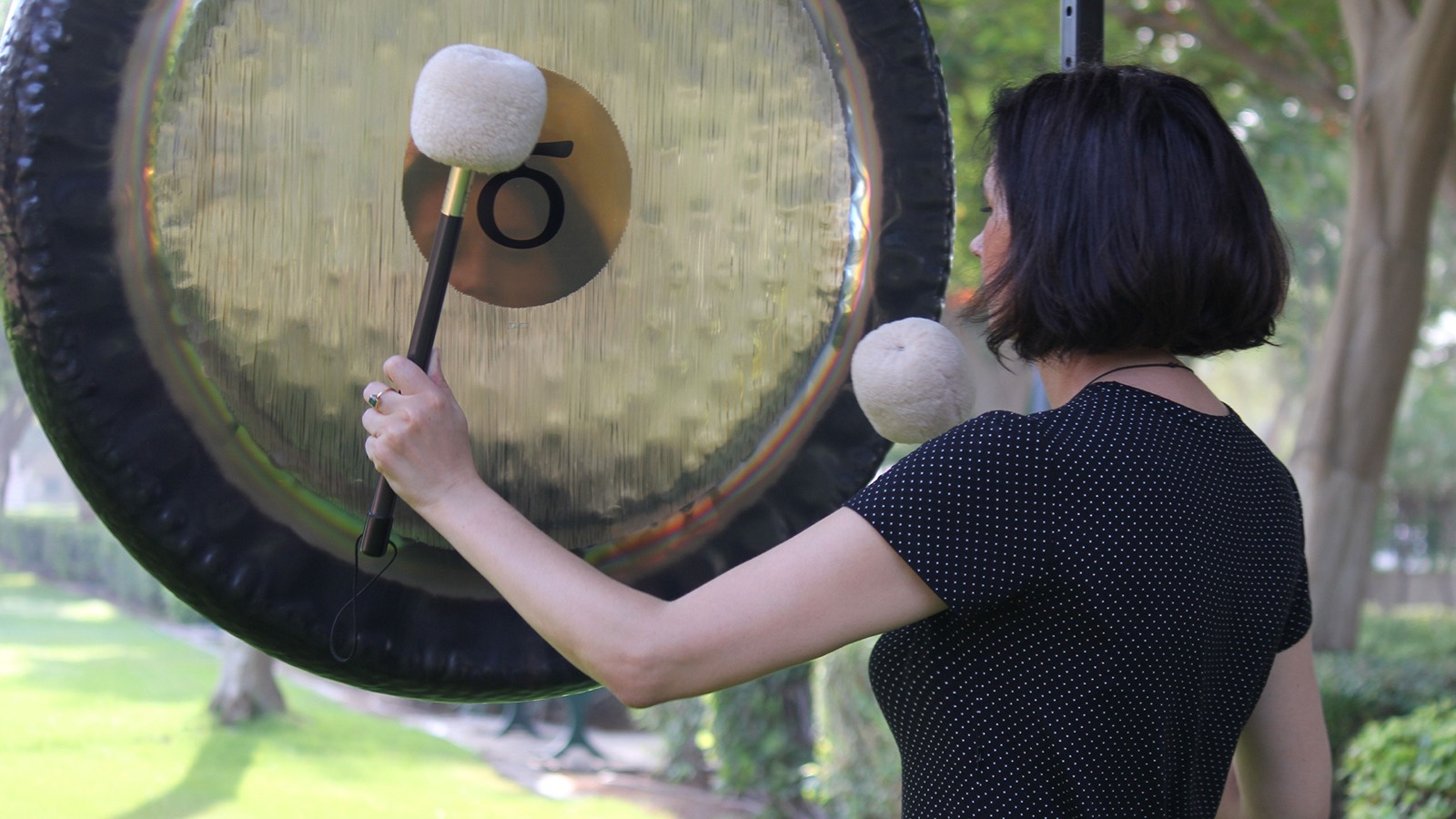 Magdalena playing a large gong outdoors
